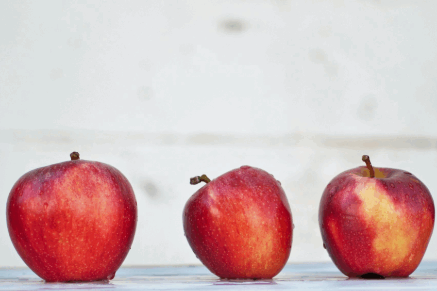 A photo of a row of red apples in a horizontal line on a white background. The other visible ones are in a uniform rounded shape and size, but the one in the middle is slightly crooked.