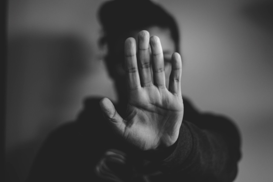 black and white photo of a person holding a hand up to the camera in a "stop" gesture with palm facing outwards and all fingers stretched up. The outstretched hand covers the person's face with dept of field perspective.