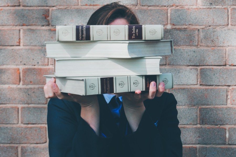 A person holding up thick academic leather bound books in a small stack in front of their face