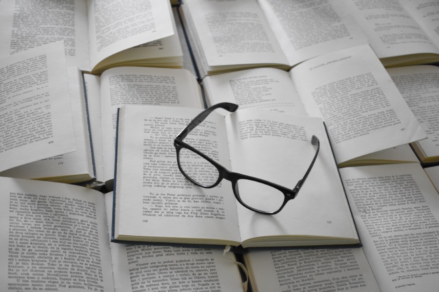 A pair of glasses sit on a pile of open books