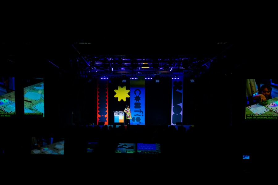 A photo of a dark auditorium room with a stage decorated with large graphic shapes including a bright yellow star above the speaker.