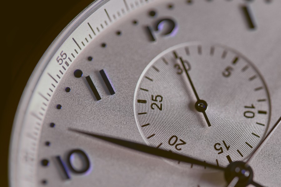 A close-up photo of a silver face wristwatch where 10, 11 and 12 are visible as well as the smaller circle for the second hand.