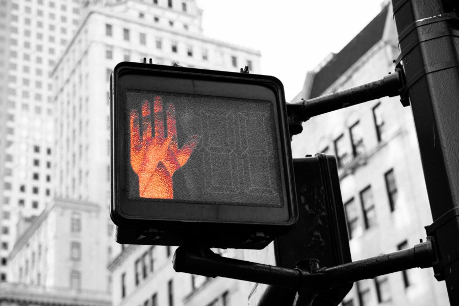 An electronic street sign displaying a red stopping hand in a busy urban city