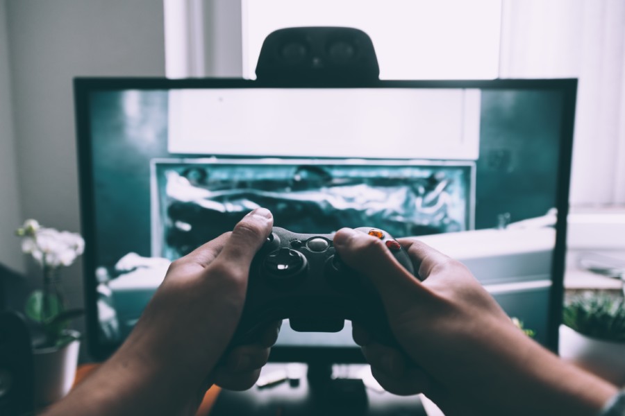 A photo of a person holding an xbox controller in front of a large desktop screen where they are playing a video game.