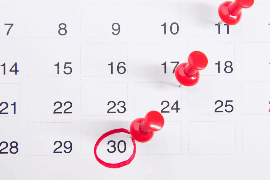 A photo of a printed calendar on white background with red plastic pins in some of the weeks and a red marker pen circle on the last day of the month.
