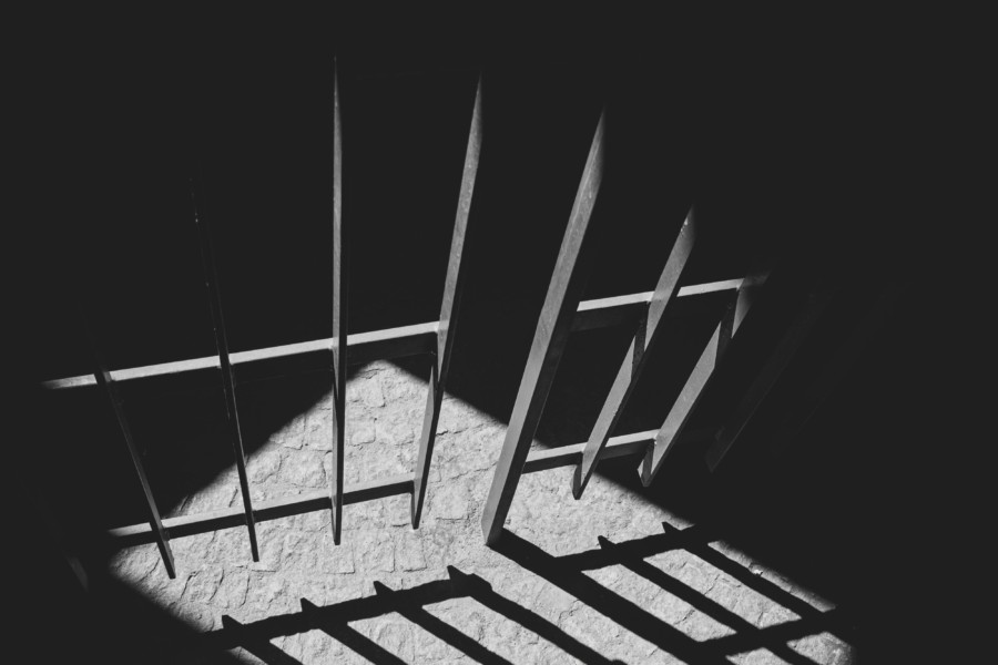 A black and white photo of a shaft of light illuminating the door of prison cell bars.