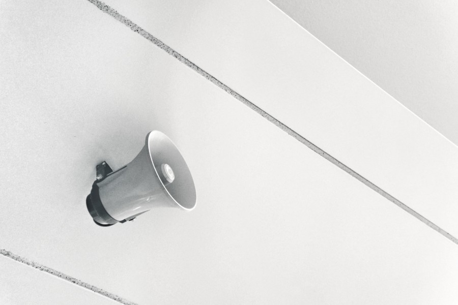 A small white megaphone attached to a white wall ready to play audio information and warnings.