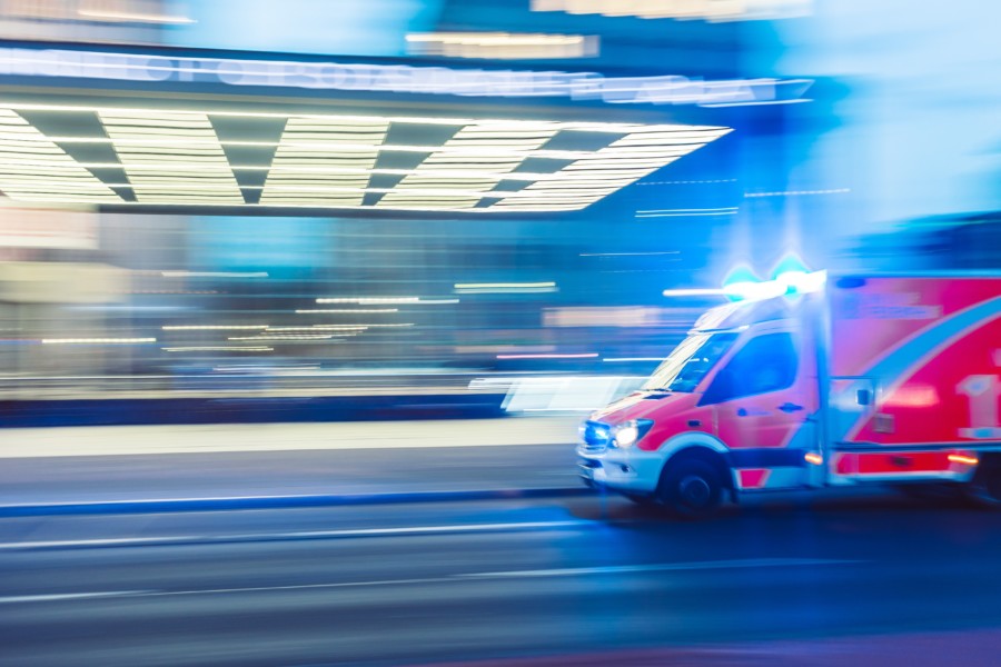 A photo of an ambulance rushing past on a road where the rest of the background street is blurred horizontally to show fast paced movement