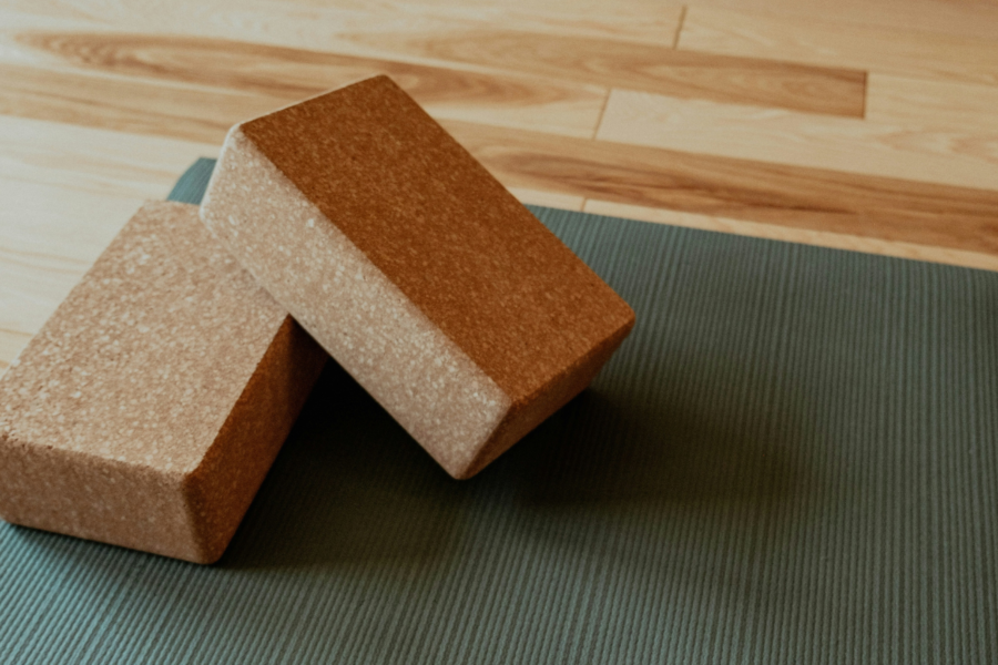 A photo of a green yoga mat with some brown cork blocks sat on top, on a wooden studio floor.
