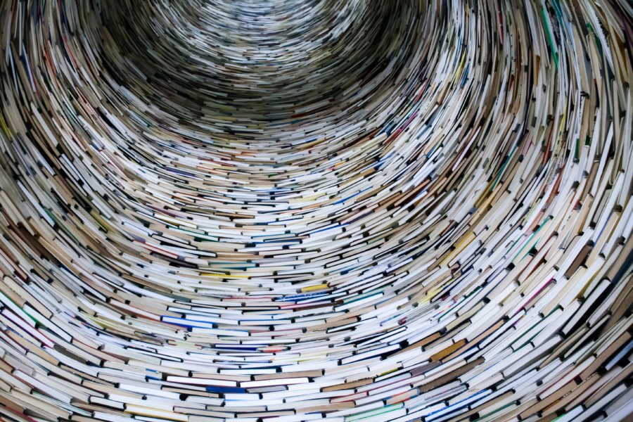 A photo of a cylindrical tower of books piled on top of each other like bricks. Some of the height has been mirrored to seem taller than it actually is.