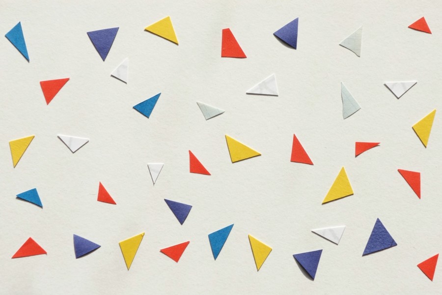 A collection of multi-coloured triangular shaped pieces of paper arranged with equal gaps between them on a white background. The triangles show the corners have been cut form something.