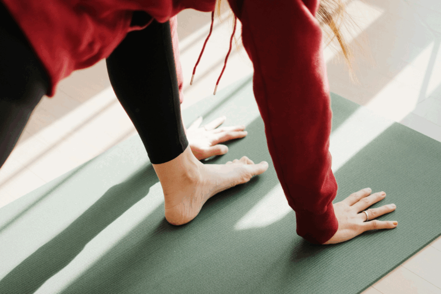 A photo of a person in red jumper and black leggings doing a kind of forward lunge pose in yoga on a green yoga mat.