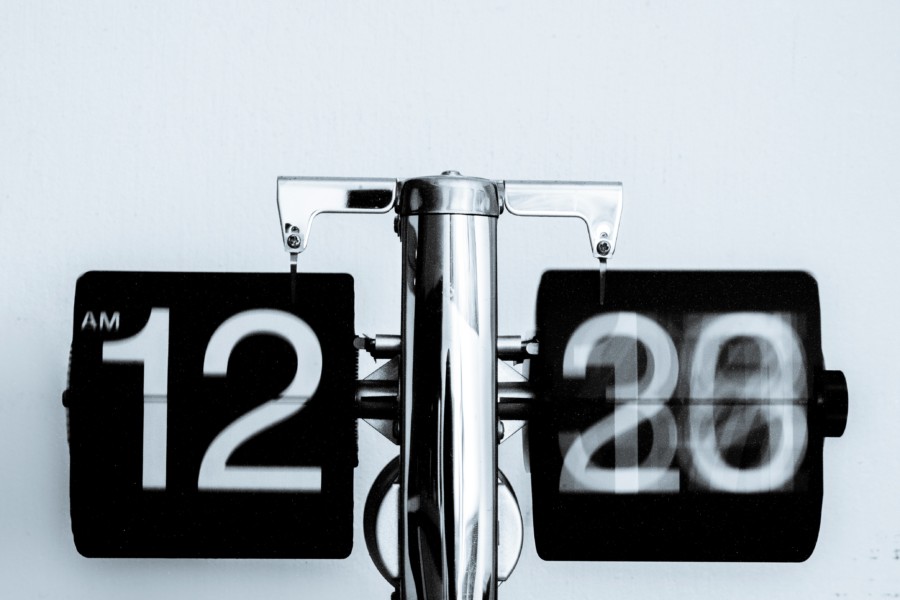 A black and white photo of a clock where the numbers flip over to reveal the next number. The number on the left is 12, while the camera effect creates a motion blur on the minute side to indicate the passage of time.