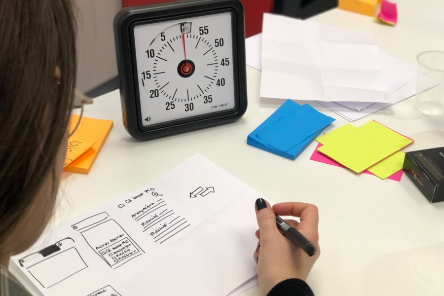 A person writing on a piece of paper surrounded by post-it notes with a square black clock indicating a timed session of work.
