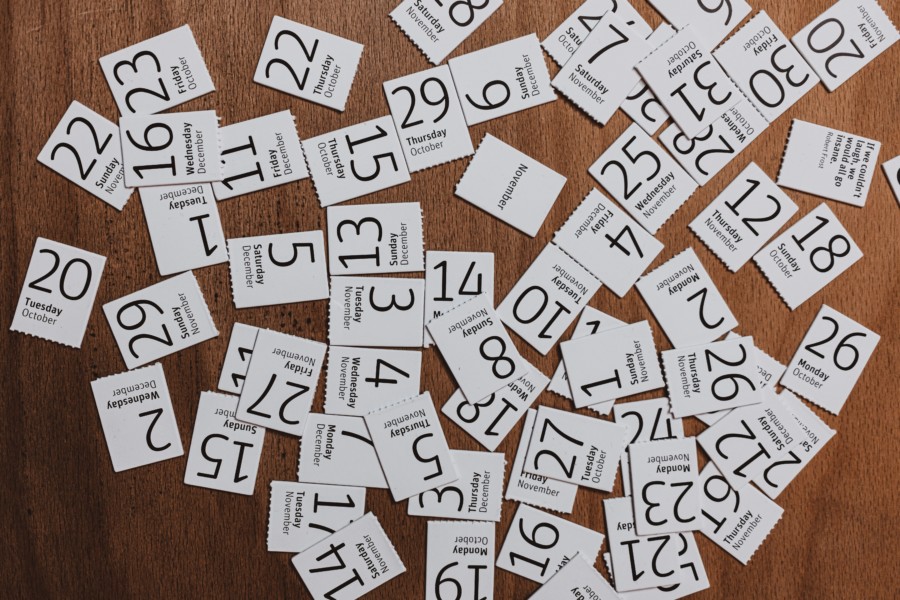 On a wooden desk there is a large scrambled array of minimal white cards with random dates of the year written in large modern black text on each.