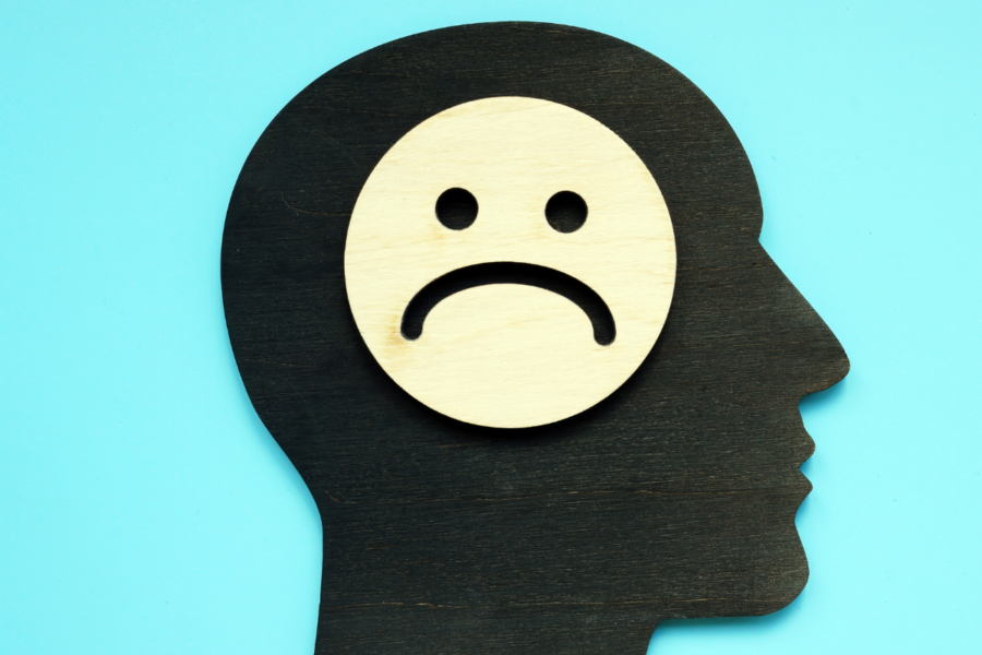 A graphic design silhouette of a person's head on a bright blue background where a white circle with black simple sad face is placed on the head.