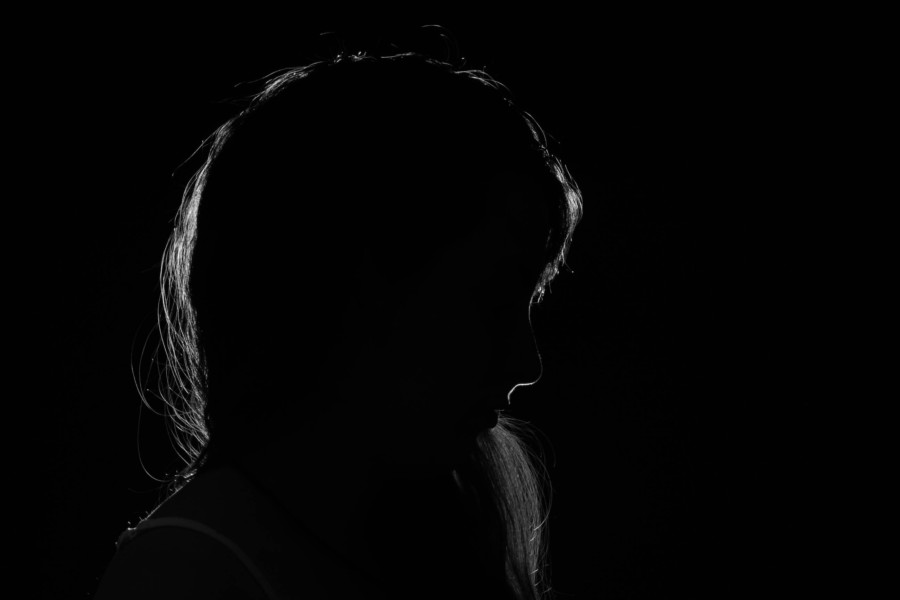 A faint silhouette of a persons head slightly bowed in the darkness creates a sense of shame.