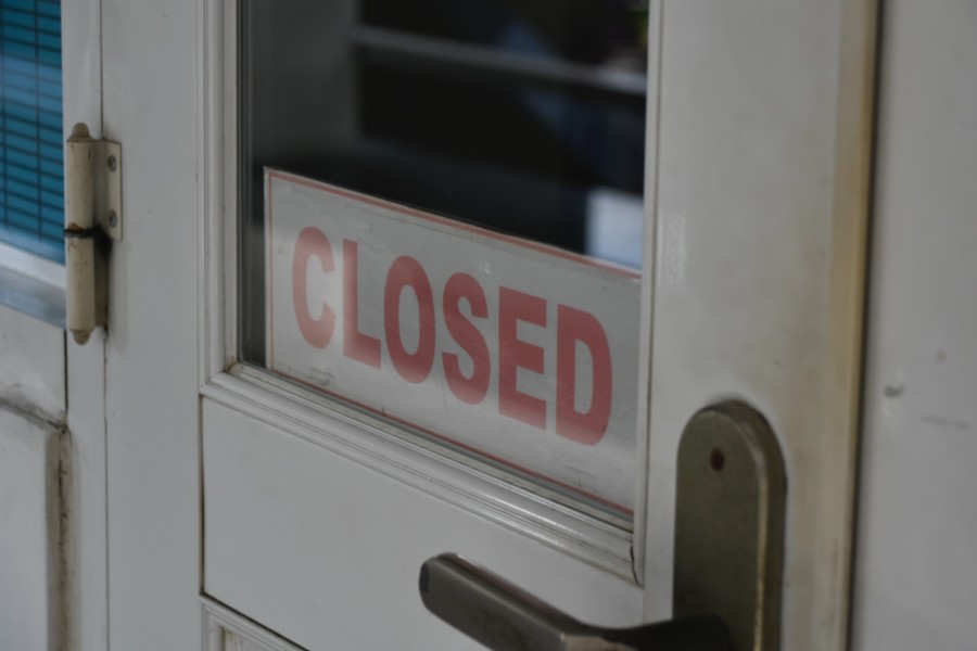white sign in window of a white wooden door with CLOSED in red capital letter font