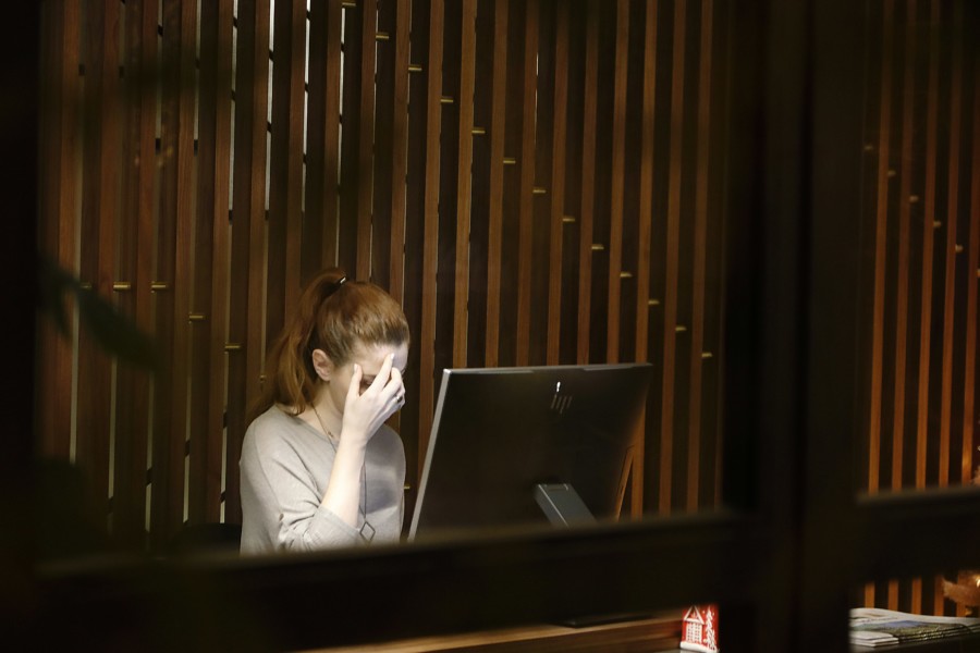 A person sat at a computer holds their hand over their face in overwhelm.