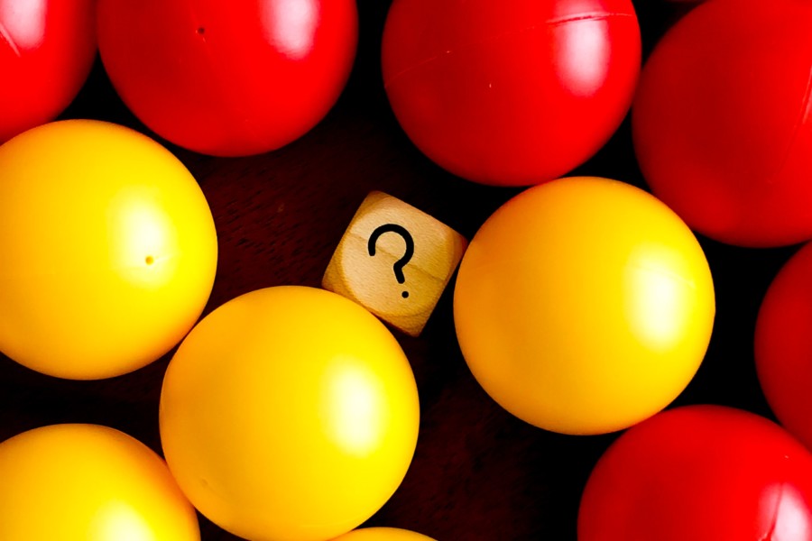 A collection of brightly coloured balls sit in either corner of the photo with a wooden block that has a black question mark on it in the centre.