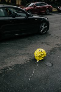 a rather sorry-looking yellow smiley face balloon has drifted down to the ground and nearly got caught in traffic - but is still smiling...