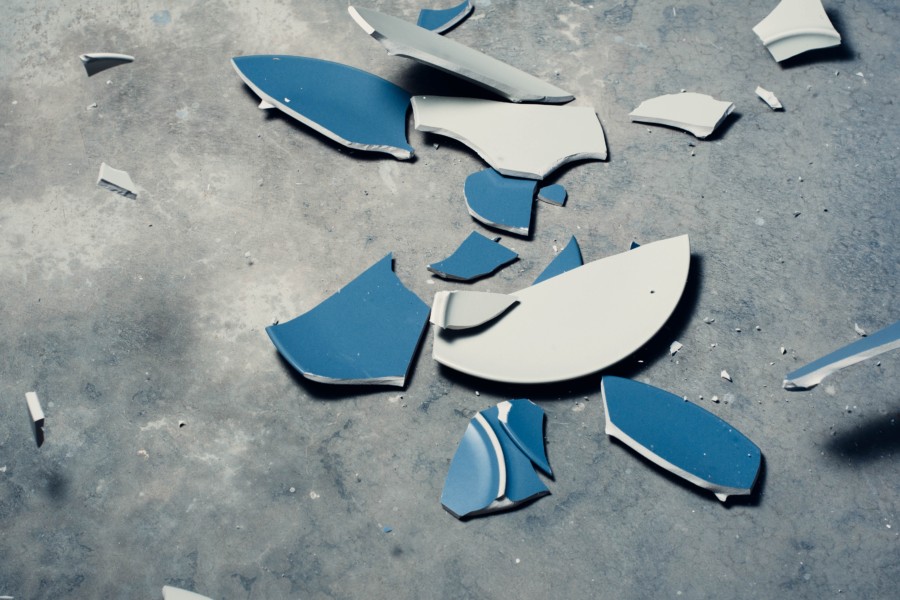 a broken ceramic plate where both blue and white sides are visible in the shattered pieces spread around a grey concrete floor