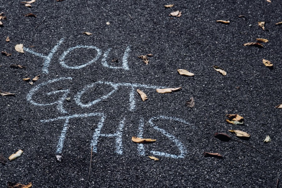 "You got this" is written in chalk capitals on a tarmac/asphalt road covered in autumnal leaves.