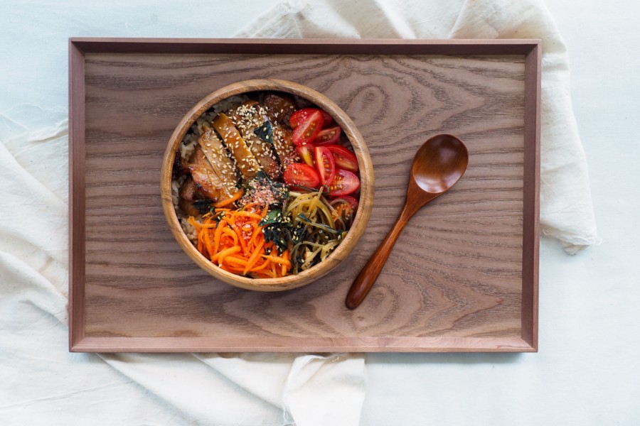A tightly packed wooden bowl of mixed chopped veg and meat is on a wooden tray with a little wooden spoon ready to eat, fuel and nourish the consumer.