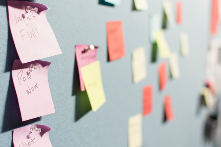 A light grey pinboard is covered in multi-colour post-it notes with various short handwritten notes on them.
