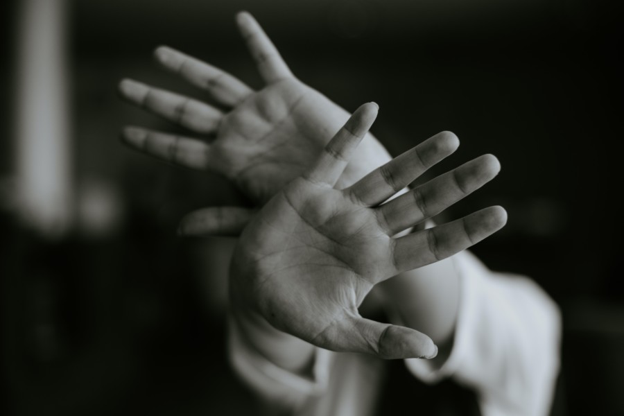 black and white photo of a person crossing both hands over each other in a stopping gesture with palms facing outwards to the camera and covering the person's face