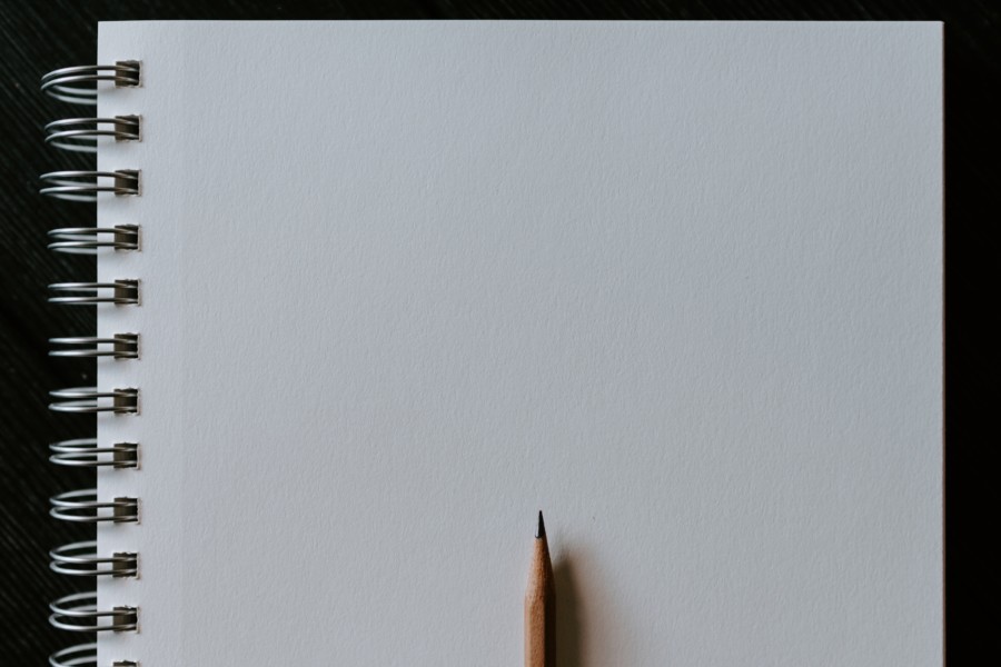 A blank white spiral notebook is open with a pencil sat on top and pointing upwards at the bottom of the image