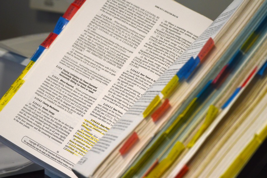An open book with 2 columns of small text suggesting a textbook or academic publication. There are a variety of colourful tabs stuck into each page at different heights with notes on the content.