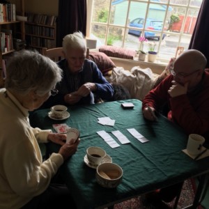 Photo of 3 people playing cards and drinking coffee. John VanEvery is in the centre.