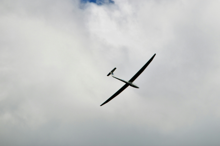 A photo of a glider plane with long horizontal wings floating on the wind in a cloudy sky