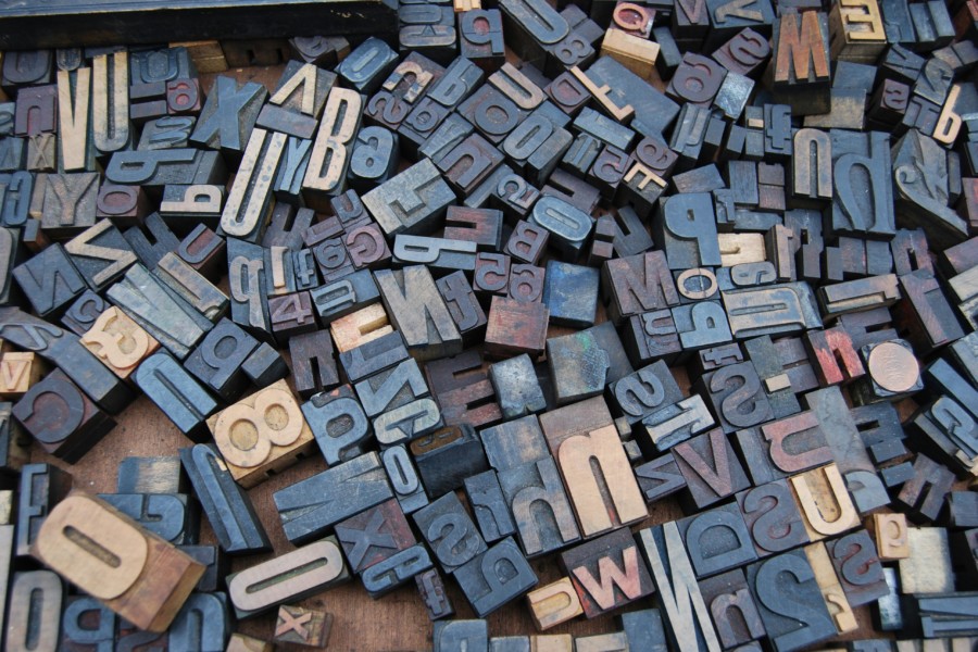 A full screen photo of different font and size metal letter blocks used in an old printing press, arranged in a jumbled but flat layout.