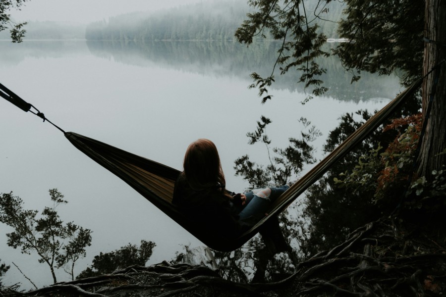 A photo of a person sat in a hammock next to a lake.