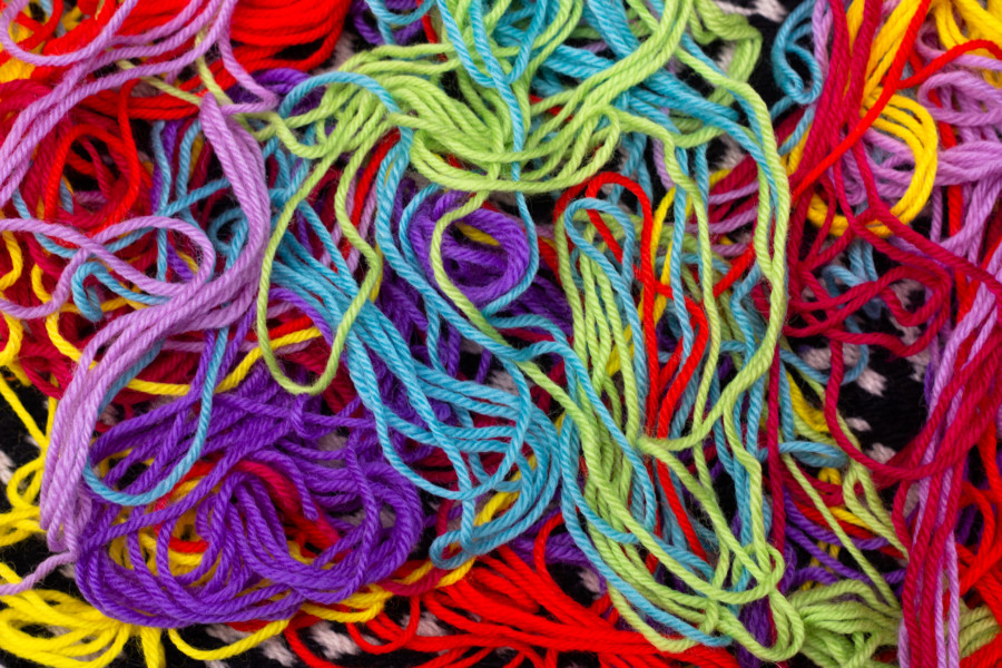 A close up photo of various threads of brightly coloured wool all loosely tangled into a pile.