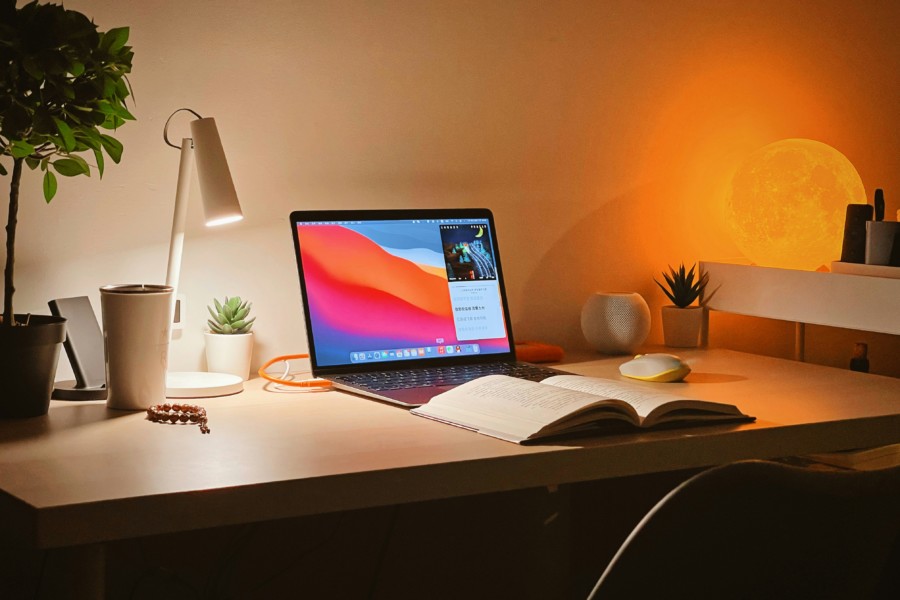 A desk space with open laptop lit by the warm glow of a spherical lamp with the moon's surface pattern.